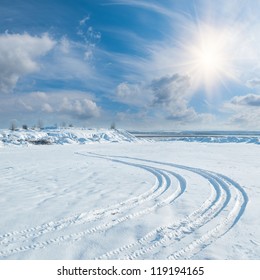 Winter Landscape With Tire Trace On Snow Leaving To The Horizon, Sun And Clouds In Sky