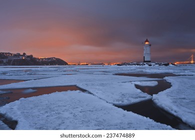 Winter landscape with a view of the lighthouse, iced sea and night city lights