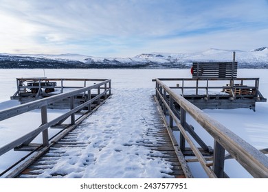 Winter landscape with wooden boat dock covered in snow in front of an icy snow-covered lake in Swedish Lapland - Powered by Shutterstock