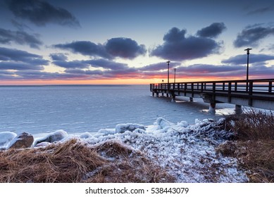 Winter landscape. Wooden pier and frozen Baltic Sea at sunset time on Hel Peninsula. Poland, Europe.