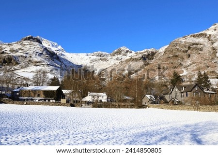 Winter in the Langdale Valley of England's Lake District National Park. The hamlet at the foot of the mountain and the fells are covered in snow with a beautiful clear blue sky.