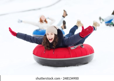 Winter, Leisure, Sport, Friendship And People Concept - Group Of Happy Friends Sliding Down On Snow Tubes