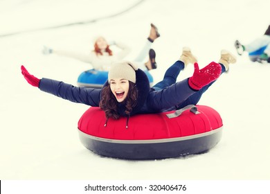 Winter, Leisure, Sport, Friendship And People Concept - Group Of Happy Friends Sliding Down On Snow Tubes