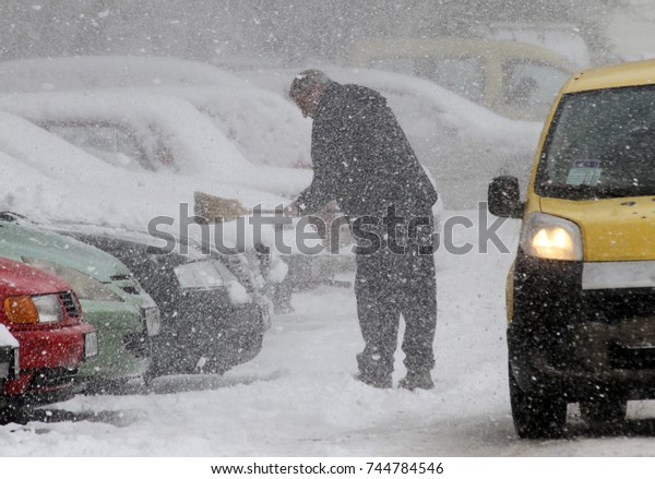  Winter, A man with a broom\
cleans car from snow on the street in a big snowstorm in Sofia,\
Bulgaria - Jan 7, 2013, car pass near by man, all cars are under\
snow 