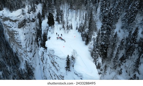 Winter mountain cliff covered by snow, ice, and fur trees. Clip. Stunning frozen winter nature, aerial view of tourists enjoying the day on the cliff edge. - Powered by Shutterstock