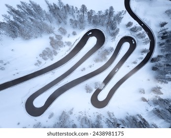 Winter in the mountains: perpendicular view of a curved mountain road with few cars forming loops. Snow-covered trees and surroundings. Italy, Dolomites, road to Passo Rolle pass. - Powered by Shutterstock