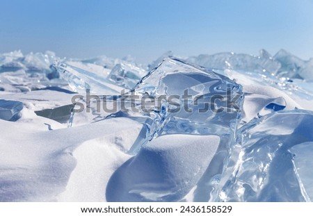 Winter natural background with fragments of blue snowy ice and heaps of pieces of ice floes on frozen Baikal Lake on sunny frosty day. Abstract cold background. Harsh lifeless north environment