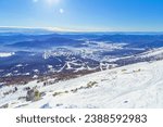 Winter nature panorama with Sheregesh ski resort in Altai, Russia, picturesque nature, sun flare on blue sky, white snow slopes and ski track, top view with range mountains, forest, aerial perspective