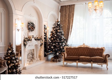 Winter New Year And Christmas Decoration In White Large Living Room. Decorated Christmas Tree Near Baroque Sofa And Classical Fireplace In Hall.