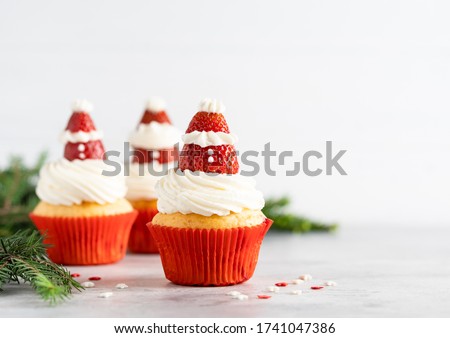 Winter and new year cupcakes in red paper cups with creamy frosting and strawberry santa clause on the top. Christmas dessert, new year cooking. Copy space. White background.