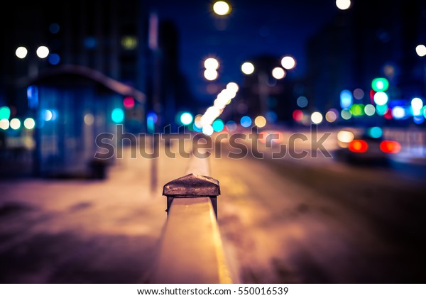 Winter night in the big city, the\
bus stop and road with car. Close up view from the handrail on the\
sidewalk level, image vignetting and the yellow-blue\
toning