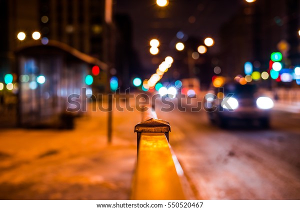 Winter\
night in the big city, the bus stop and the stream of cars. Close\
up view from the handrail on the sidewalk\
level
