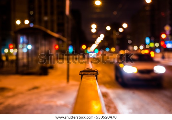 Winter night\
in the big city, the bus stop and next passing car. Close up view\
from the handrail on the sidewalk\
level