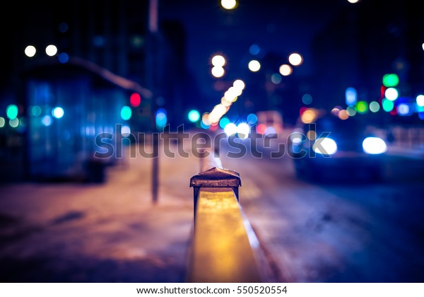 Winter night in the big city,\
the bus stop and the stream of cars. Close up view from the\
handrail on the sidewalk level, image vignetting and the\
yellow-blue toning