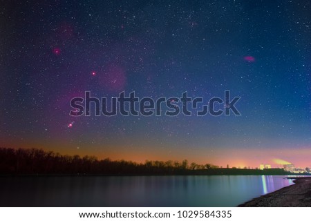 Winter night sky with Barnard’s Loop, the Orion Nebula, the Flame Nebula, the Rosette Nebula, the California Nebula, and the Pleiades as seen from the shore of the river Rhine at Mannheim in Germany.