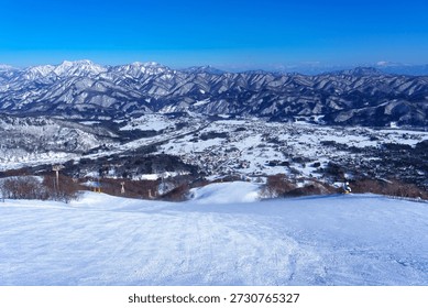 Winter panoramic view from Happo-One Ski Resort in Hakuba, Nagano Prefecture, Japan. Snow-covered mountain ridges stretch endlessly into the distance under a clear blue sky, overlooking the Hakuba Valley and surrounding villages. The expansive alpine landscape, pristine ski slopes, and dramatic mountain scenery make this image ideal for winter travel, skiing, outdoor adventure, nature, and seasonal background concepts.