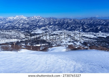 Winter panoramic view from Happo-One Ski Resort in Hakuba, Nagano Prefecture, Japan. Snow-covered mountain ridges stretch endlessly into the distance under a clear blue sky, overlooking the Hakuba Valley and surrounding villages. The expansive alpine landscape, pristine ski slopes, and dramatic mountain scenery make this image ideal for winter travel, skiing, outdoor adventure, nature, and seasonal background concepts.