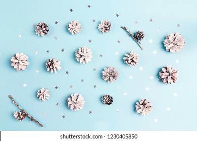 Winter Pattern With Snow Painted Pine Cones And Silver Stars On Blue Background. Top View, Flat Lay.