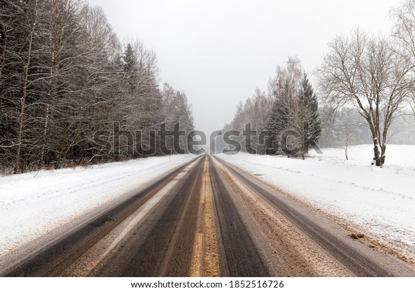 winter paved road with ruts from cars in winter,\
covered with snow after snowfall, on the surface of the paved road\
melting snow