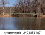 Winter photo of the green suspension bridge with trees and leaves in Stewart Park at the south end of Cayuga Lake, Ithaca New York.	