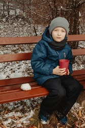 Winter Picnic Delight: 8-Year-Old Boy Savoring Tea On Snowy Bench In Rural Park. An 8-year-old Boy Enjoying A Delightful Moment On A Snow-covered Bench In A Tranquil Rural Park.