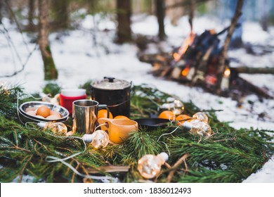 Winter picnic in the snow near by campfire with oranges and tea. Christmas garlands on fir branches