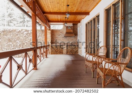 Winter plot. Two rattan wicker chairs sit on an empty veranda. White snow lies on the railing and the floor