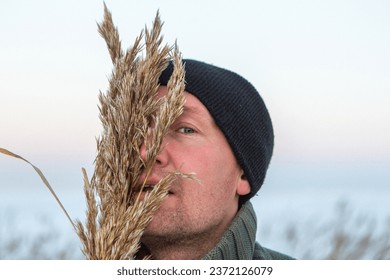 Winter portrait of handsome man in hoarfrosted grass. Winter season. snowy reeds. Soft blue sky background.