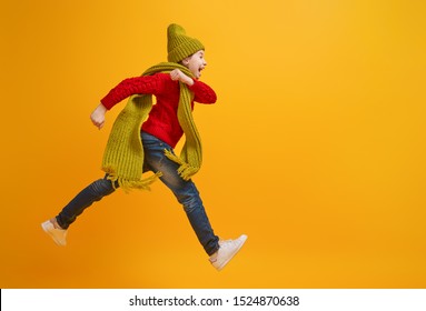 Winter portrait of happy child wearing knitted hat, snood and sweater. Girl having fun, playing and laughing on yellow background. Fashion concept.
