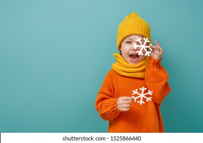 Winter Portrait Of Happy Child Wearing Knitted Hat, Snood And Sweater. Girl Having Fun, Playing And Laughing On Teal Background. Fashion Concept.