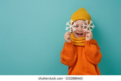 Winter portrait of happy child wearing knitted hat, snood and sweater. Girl having fun, playing and laughing on teal background. Fashion concept.                               