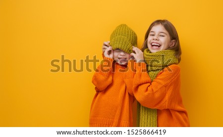 Winter portrait of happy children wearing knitted hat, snood and sweaters. Girls having fun, playing and laughing on yellow background. Fashion concept.
