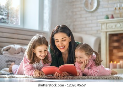 Winter Portrait Of Happy Loving Family. Pretty Young Mother Reading A Book To Her Daughters At Home.