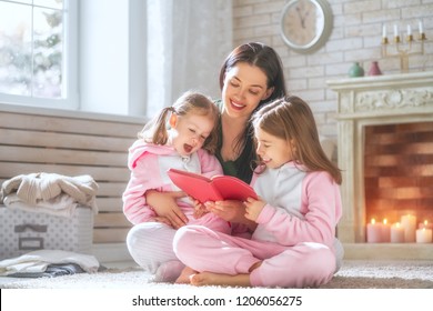 Winter Portrait Of Happy Loving Family. Pretty Young Mother Reading A Book To Her Daughters At Home.