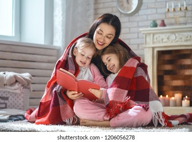 Winter Portrait Of Happy Loving Family. Pretty Young Mother Reading A Book To Her Daughters At Home.