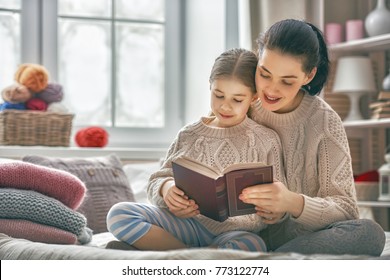 Winter Portrait Of Happy Loving Family. Pretty Young Mother Reading A Book To Her Daughter At Home.