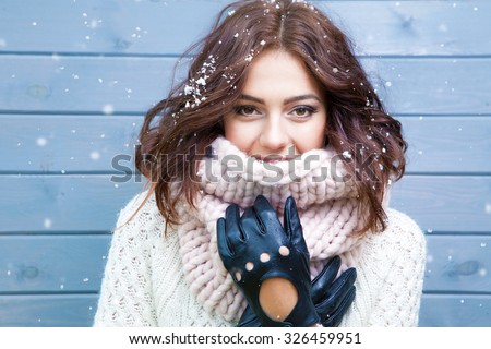 Winter portrait of young beautiful brunette woman wearing knitted snood covered in snow. Snowing winter beauty fashion concept.
