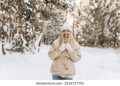 Winter portrait young beautiful woman with blond hair dressed in warm clothes with a knitted hat, smiling. Blurred snowy forest in the background - Powered by Shutterstock