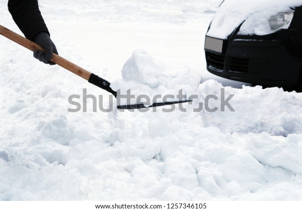 Winter problems of car drivers. Man with shovel\
clears snow around car in parking lot in winter after snowfall.\
Shovel in hand.