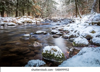 Winter River Scene In The Forest As Snow Covers Rocks Along The Peaceful River 