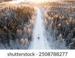 A winter road cutting through a snow-covered forest, captured from above with a RV, motorhome, traveling down the isolated path at sunset.