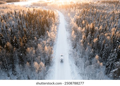 A winter road cutting through a snow-covered forest, captured from above with a RV, motorhome, traveling down the isolated path at sunset. - Powered by Shutterstock