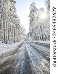 Winter road. Wide angle image of a road through a winter forest on a sunny day. Snow-capped trees and road covered with ice.