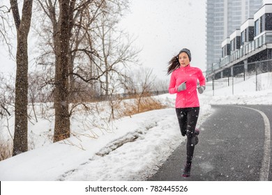 Winter Running Asian Girl Wearing Cold Weather Clothing For Outside Exercise In Snow Storm Snowfall During Winter Training Outdoors In City Street. Fitness Woman Exercising.