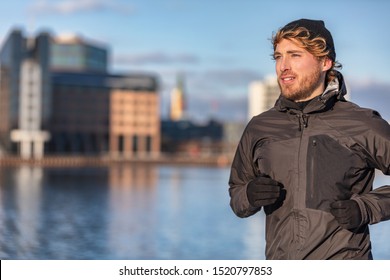 Winter running athlete man jogging outdoor in city outside wearing cold weather accessories - hat ,gloves , windproof sport jacket. Active healthy lifestyle.