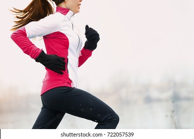 Winter running athlete woman on cold run jogging fast with speed and sprint on outside workout wearing warm clothing gloves, winter tights and wind jacket in snow weather.