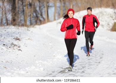 Winter Running Exercise Couple. Runners Jogging In Snow. Young Asian Woman Fitness Model And Caucasian Man.