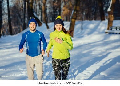 Winter Running Exercise Couple. Runners Jogging In Snow. Young Asian Woman Fitness Model And Caucasian Man.