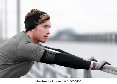 Winter Running Man Runner Training Outside Using Phone Holder Listening To Music With Headband Cold Weather Accessories Wearing Wearable Tech Smartwatch.