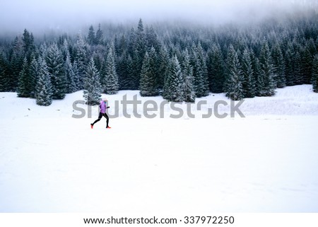 Winter running woman. Sport, fitness, jogging inspiration and motivation. Young happy woman cross country running in mountains on snow, winter day. Female trail runner working out, jogging exercising.